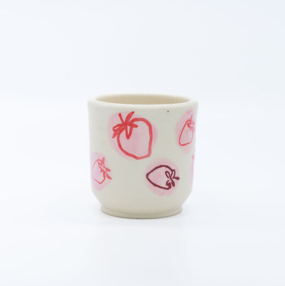 Small white cup with red strawberry patterns on a white background